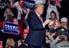 Man clapping at a rally with audience cheering.