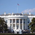 White House with American flag flying, daytime.