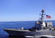 Warship sailing with American flag in open sea.