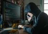 Hacker in hood using computer and phone analyzing code