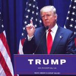 Man speaking at podium with American flags behind