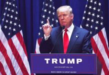 Man speaking at podium with American flags behind