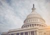 Capitol dome with American flag, under cloudy sky.