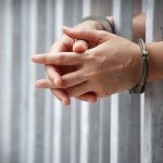 Hands in handcuffs gripping prison bars