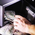 Hand putting cash into a safe.