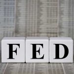 Blocks spelling FED against financial chart background.