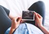 Person holding ultrasound image over pregnant belly