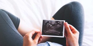 Person holding ultrasound image over pregnant belly