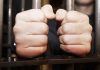 Hands gripping jail cell bars tightly
