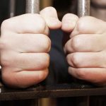 Hands gripping jail cell bars tightly