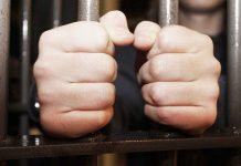 Hands gripping jail cell bars tightly