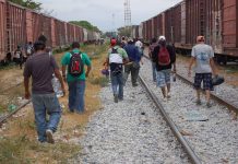 People walking along train tracks carrying backpacks
