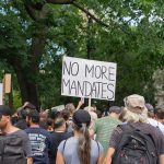 Crowd holds No More Mandates sign at protest