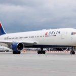 Delta Airlines airplane on airport runway, cloudy sky