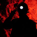 Silhouette of miner with headlamp against red background