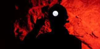 Silhouette of miner with headlamp against red background