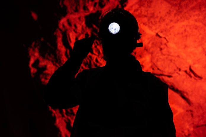 shutterstock_1937531479.jpg featured image Silhouette of miner with headlamp against red background