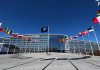 Flags outside NATO headquarters building under clear blue sky.