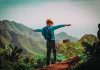 Child with backpack stands on mountain arms outstretched