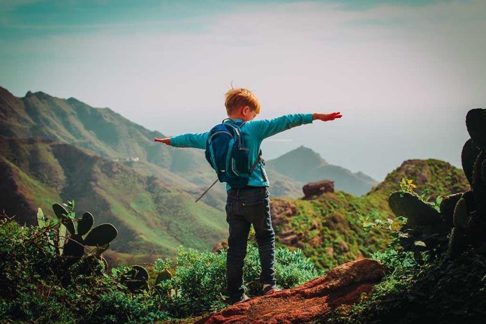 1020047392 featured image Child with backpack stands on mountain arms outstretched
