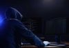 Hooded figure using dual monitors in dark room