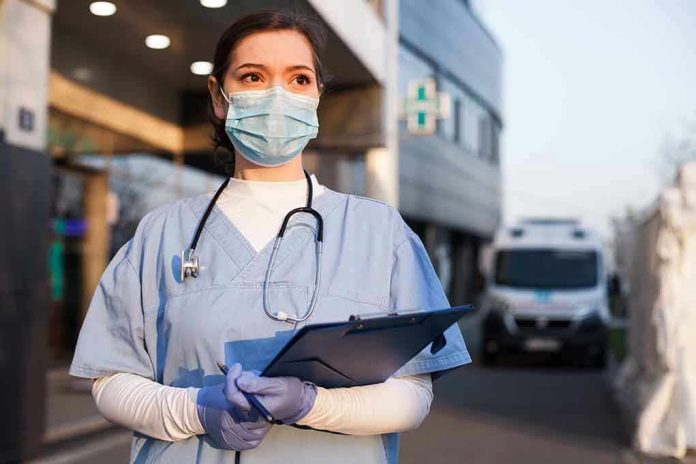 Nurse in scrubs and mask outside hospital holding clipboard