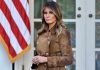 Woman in brown coat beside American flag.