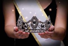 Sash-wearing person holding an ornate jeweled crown.