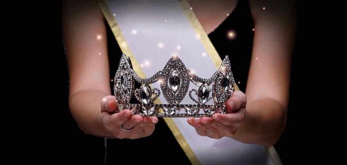 1986963572 Sash-wearing person holding an ornate jeweled crown.