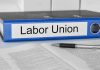 Blue binder labeled Labor Union beside papers and pen.
