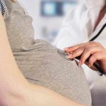 Doctor uses stethoscope on pregnant woman's belly