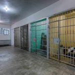 Interior view of a prison cell block with metal bars and concrete flooring