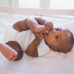 A playful baby lying in a crib, holding their feet