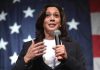 Woman speaking with microphone, American flag background.