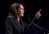 Person speaking at podium with raised finger.