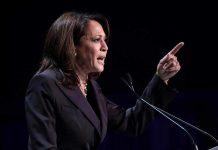 Person speaking at podium with raised finger.