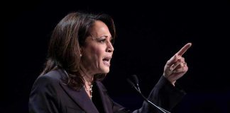 Person speaking at podium with raised finger.