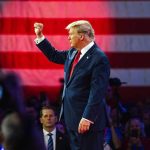 Person in suit with fist raised in front of flag.