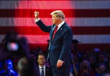 Person in suit with fist raised in front of flag.