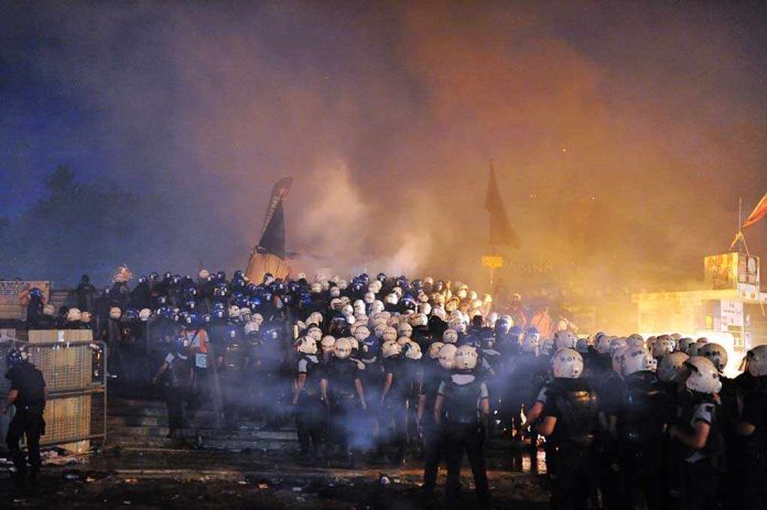 shutterstock_234178564.jpg A large crowd of police officers in helmets facing a smoky protest scene at night
