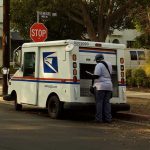 Democrats Alarmed by Proposed Changes to US Postal Service USPS mail carrier at truck near stop sign.
