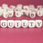 Dice spelling guilty on a red surface