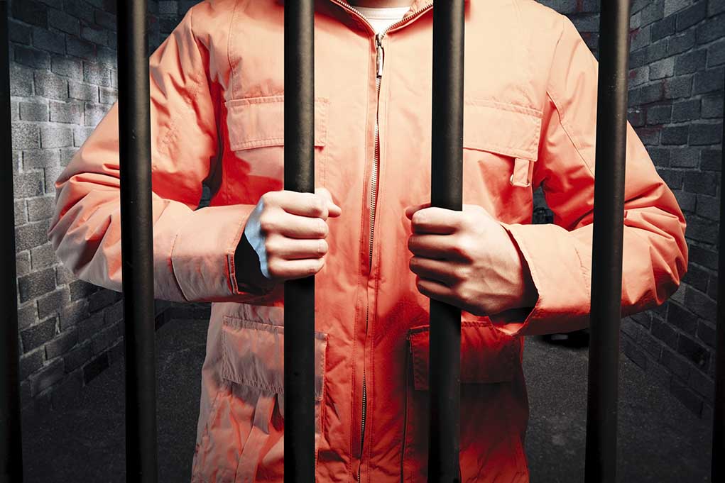 62493325 featured image Person in orange jacket behind prison bars.