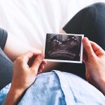 Person holding ultrasound image over pregnant belly