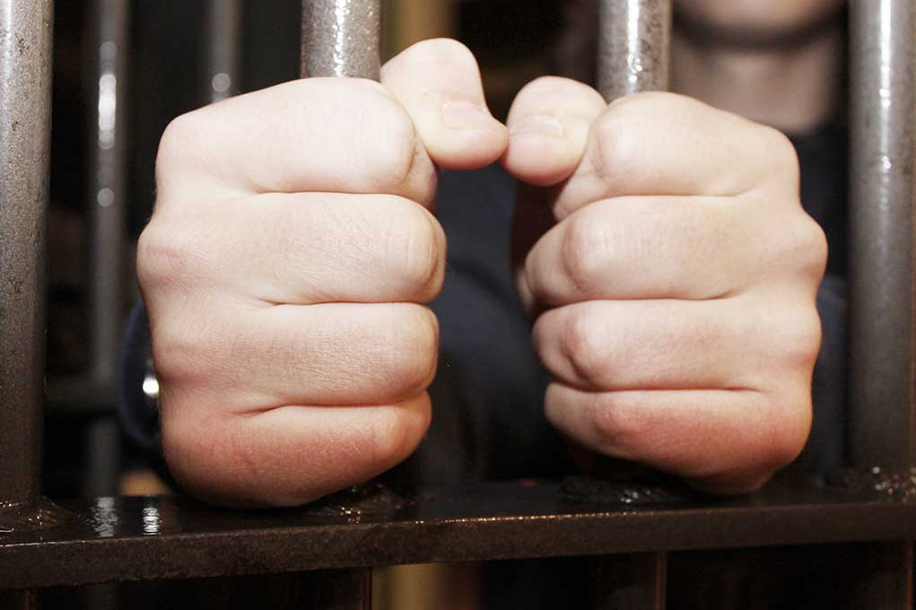 Hands gripping jail cell bars tightly