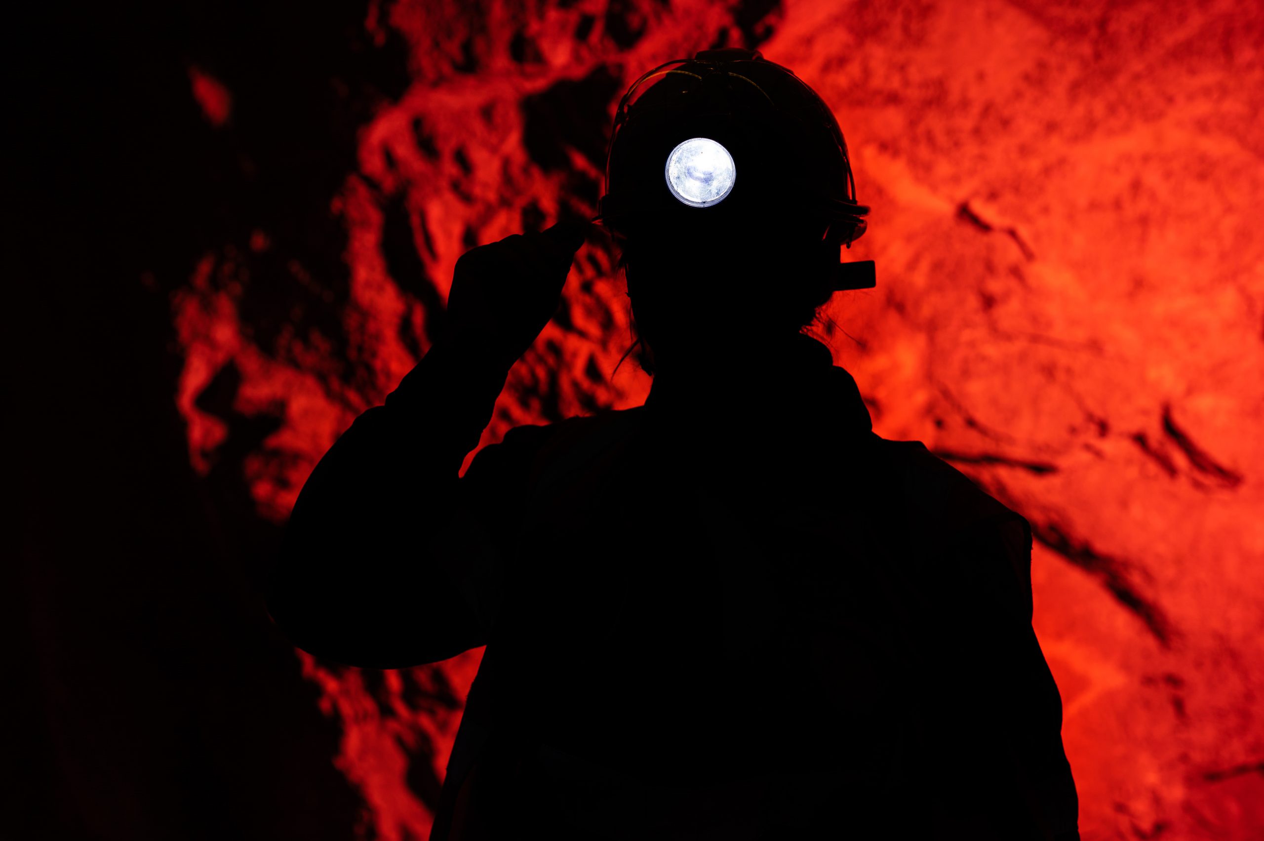Silhouette of miner with headlamp against red background