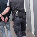 ICE Crackdown Sparks CHAOS — Activists Swarm Streets Officer escorting handcuffed person down hallway
