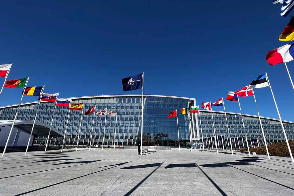 2284120437 featured image Flags outside NATO headquarters building under clear blue sky.