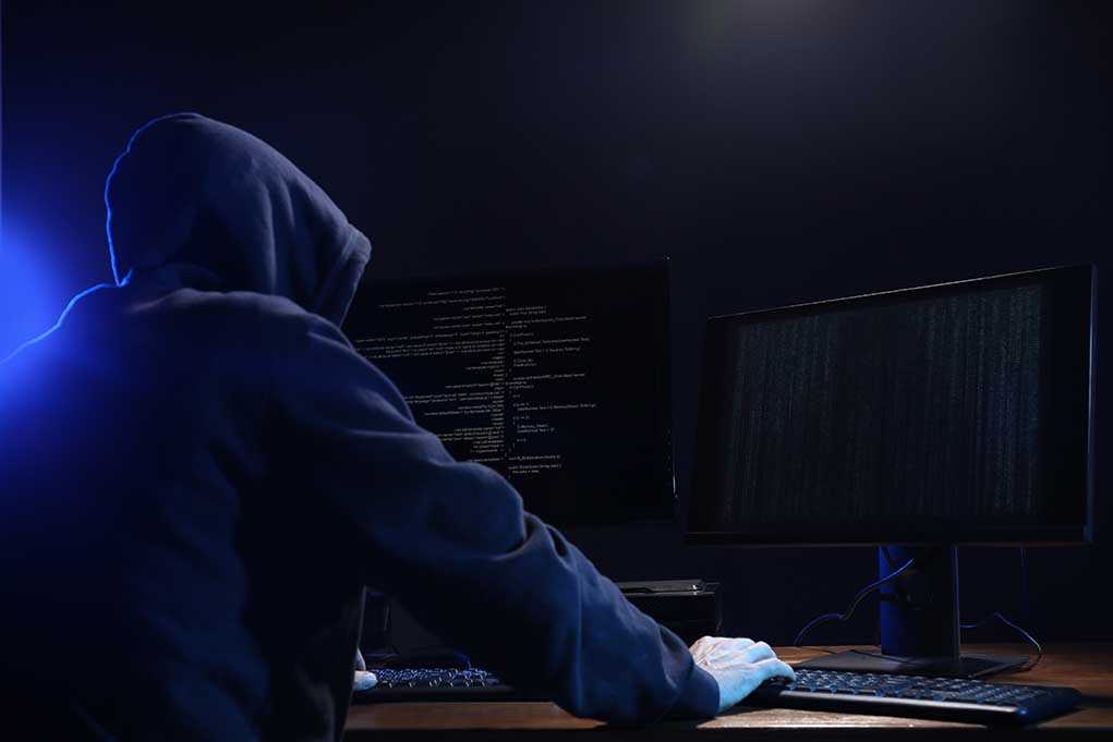 Hooded figure using dual monitors in dark room