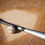 A baseball bat and ball resting on a baseball diamond